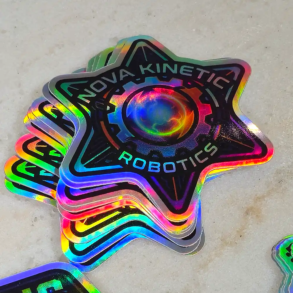 holographic-promo-stickers-1 • StickerPlanet Canada Holographic star-shaped sticker stack with 'Nova Kinetic Robotics' and a gear center design.