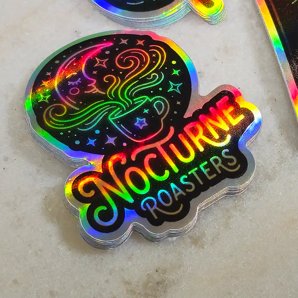 holographic-promo-stickers-5 • StickerPlanet Canada Holographic sticker with a steaming coffee cup and 'Nocturne Roasters' in rainbow lettering.